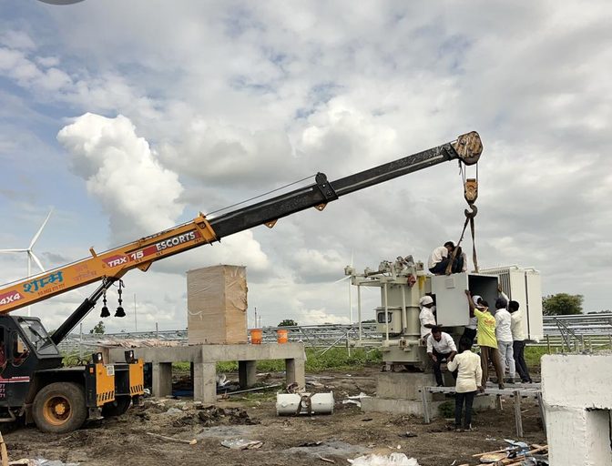 Crane lowering a transformer onto its foundation at a solar site